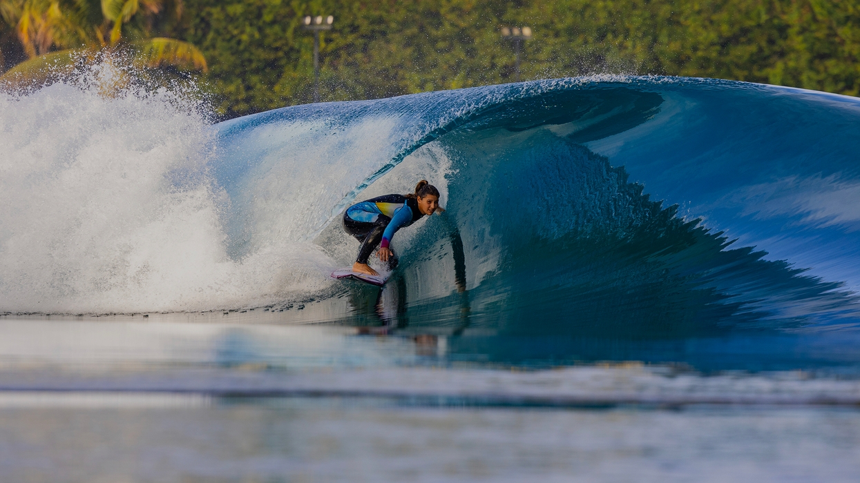 Surfer riding a perfect, curling blue wave with lush greenery in the background.
