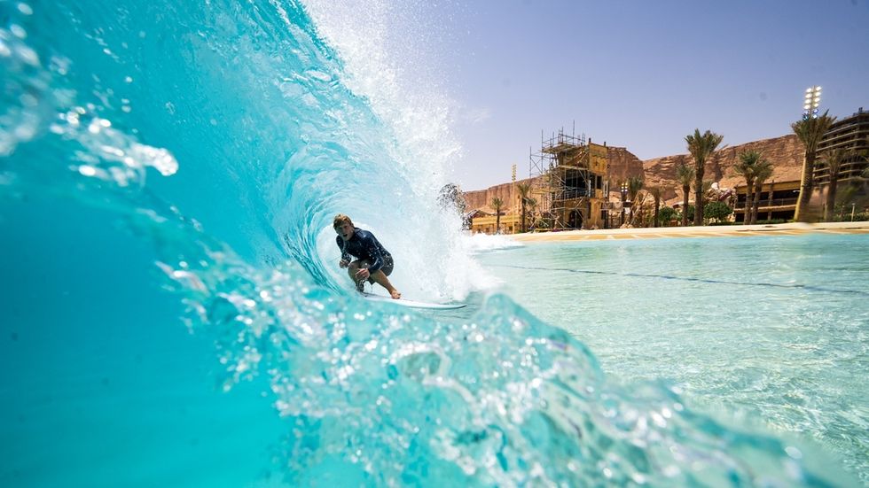 Surfer riding a turquoise wave in a sunny, desert-themed water park.