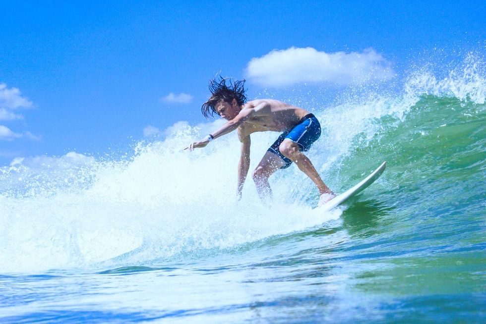 Surfer riding a wave under a clear blue sky.