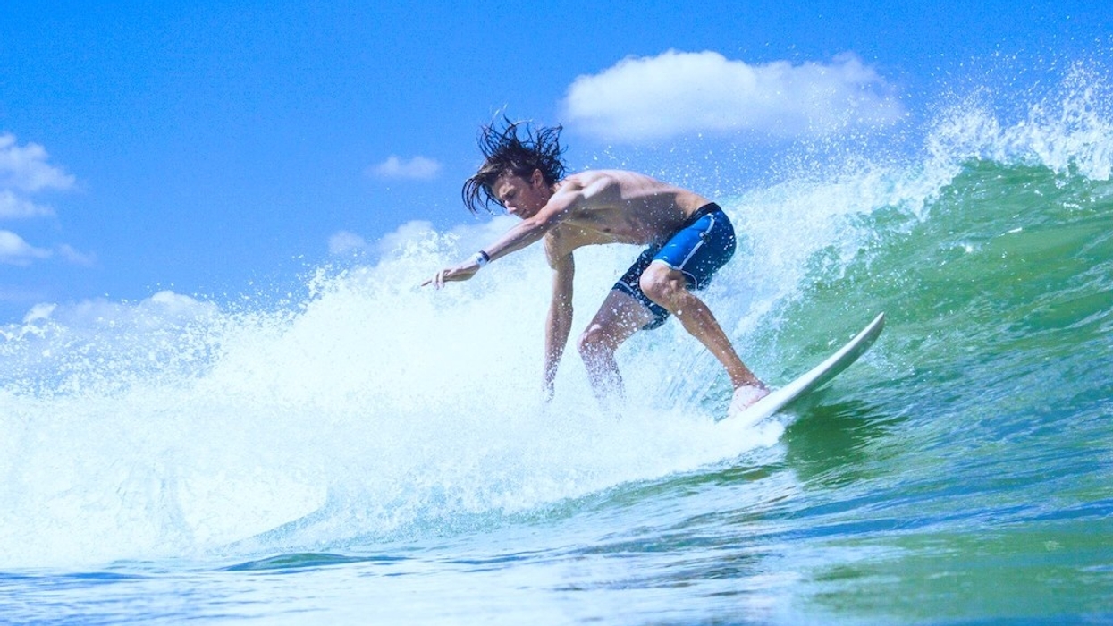 Surfer riding a wave under a clear blue sky.