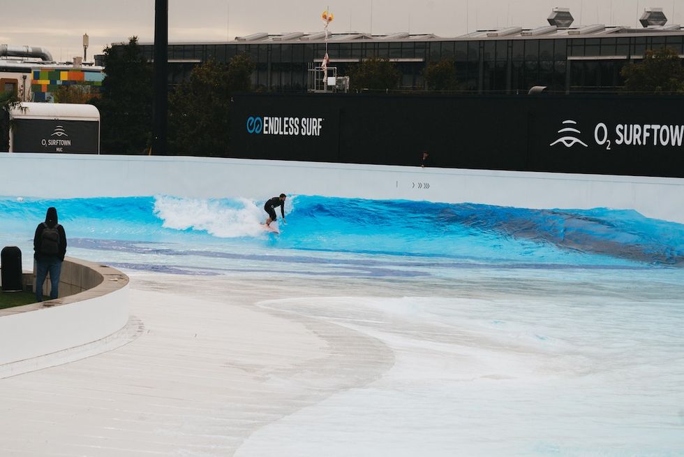 Surfer riding an artificial wave in a large, outdoor wave pool.