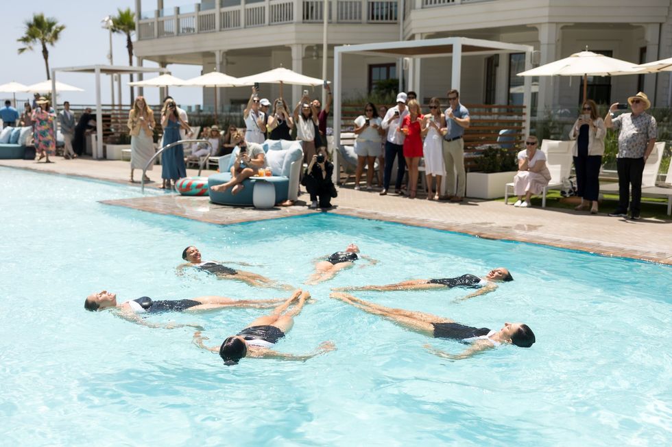 Synchronized swimmers perform in a pool, surrounded by spectators taking photos.