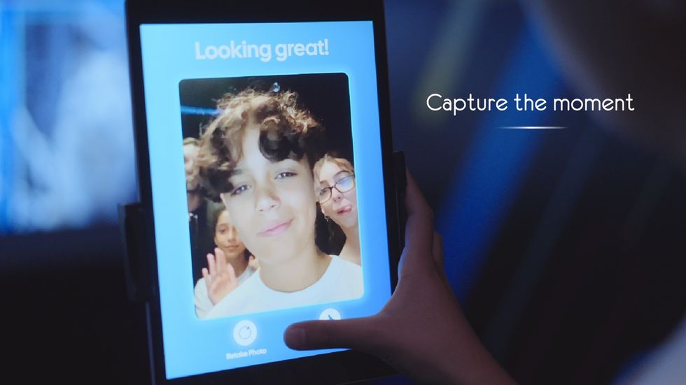 Tablet displaying a selfie of three smiling people for the Selfie Wall, with "Capture the moment" text.