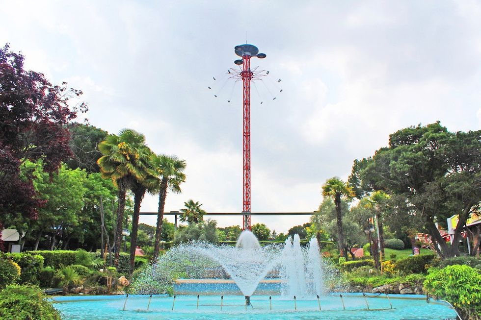 Tall amusement park ride and fountain in a lush garden setting.