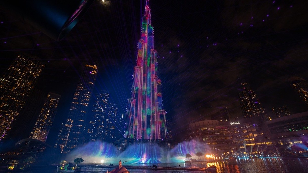 Tall building with colorful lights and water fountain in a nighttime cityscape.