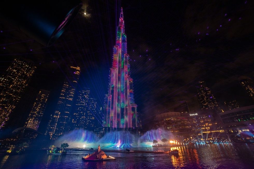 Tall building with colorful lights and water fountain in a nighttime cityscape.