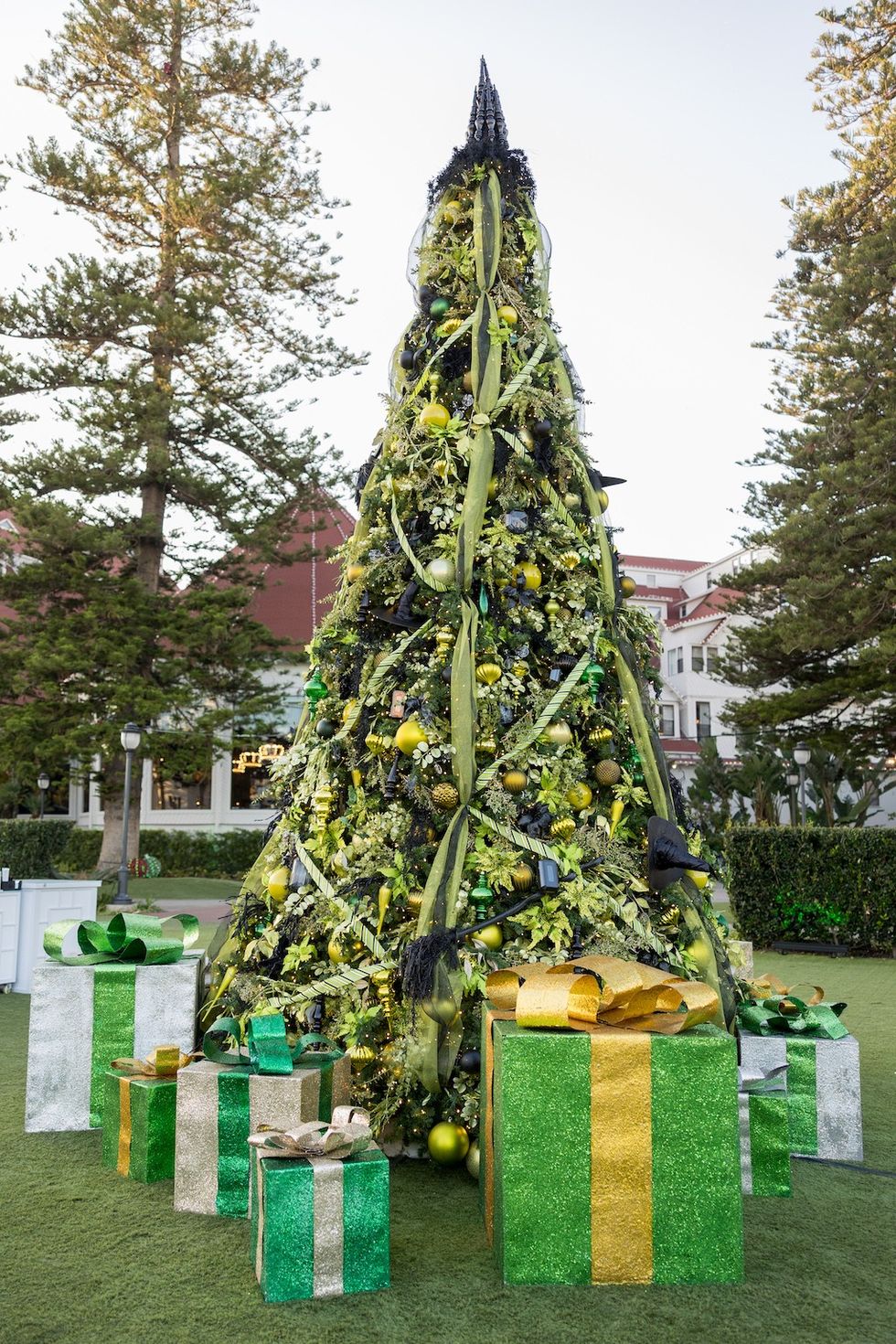 Tall, leaf-covered Christmas tree with green and gold ornaments, surrounded by gift boxes.