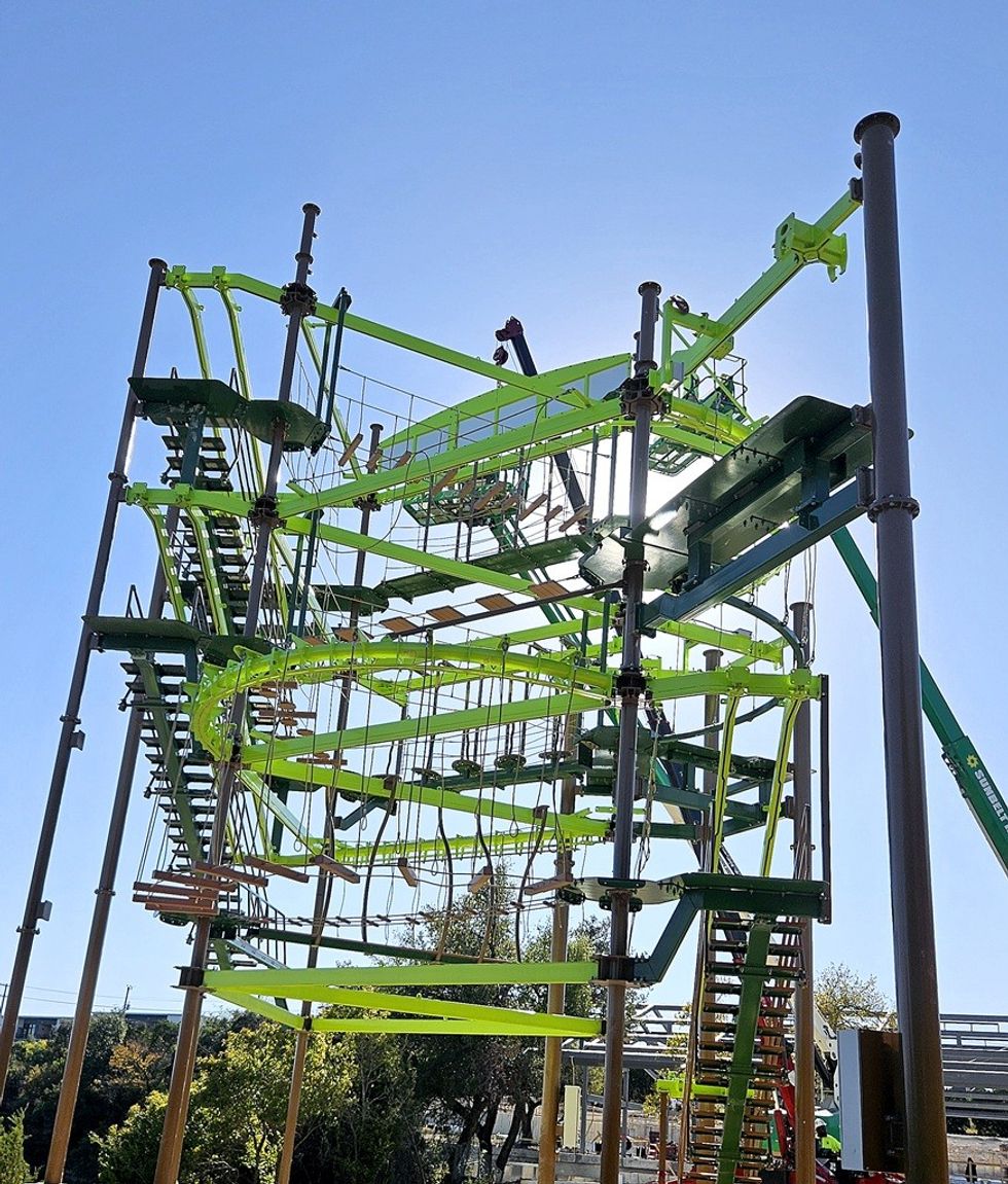 Tall outdoor ropes course with green platforms against a clear blue sky.