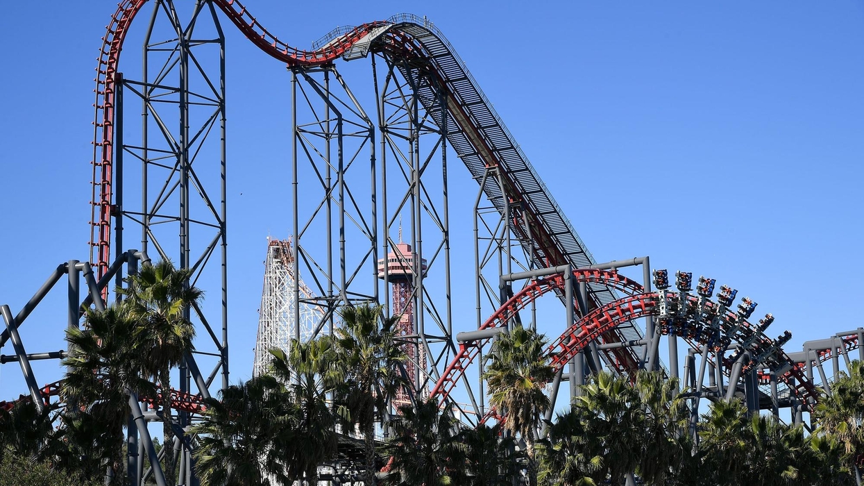 Tall steel roller coaster called X2 with red tracks and palm trees under a clear blue sky.
