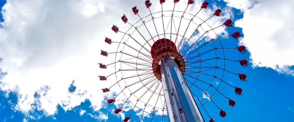 Tall swing ride against a bright blue sky with scattered clouds.