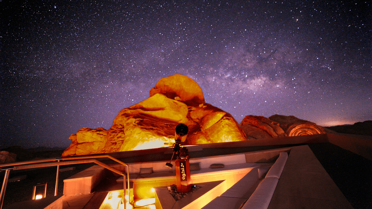 Telescope on a rooftop under a starry night sky with illuminated rock formations.