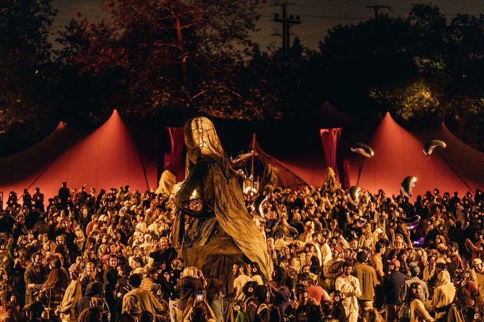 The Cort\u00e8ge: A Festive Funeral for Our Times Crowd at night outdoor festival with large sculpture and glowing headphones.