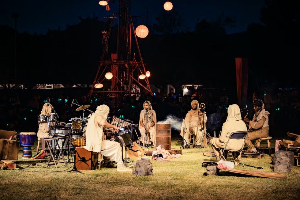 The Cort\u00e8ge: A Festive Funeral for Our Times. Group of musicians performs outdoors at night, surrounded by warm lights.