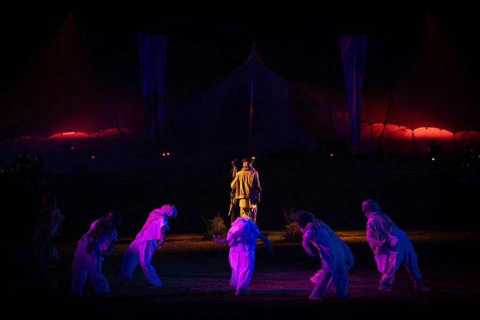 The Cort\u00e8ge: A Festive Funeral for Our Times Performers in colorful costumes on a dimly lit stage with dramatic lighting.