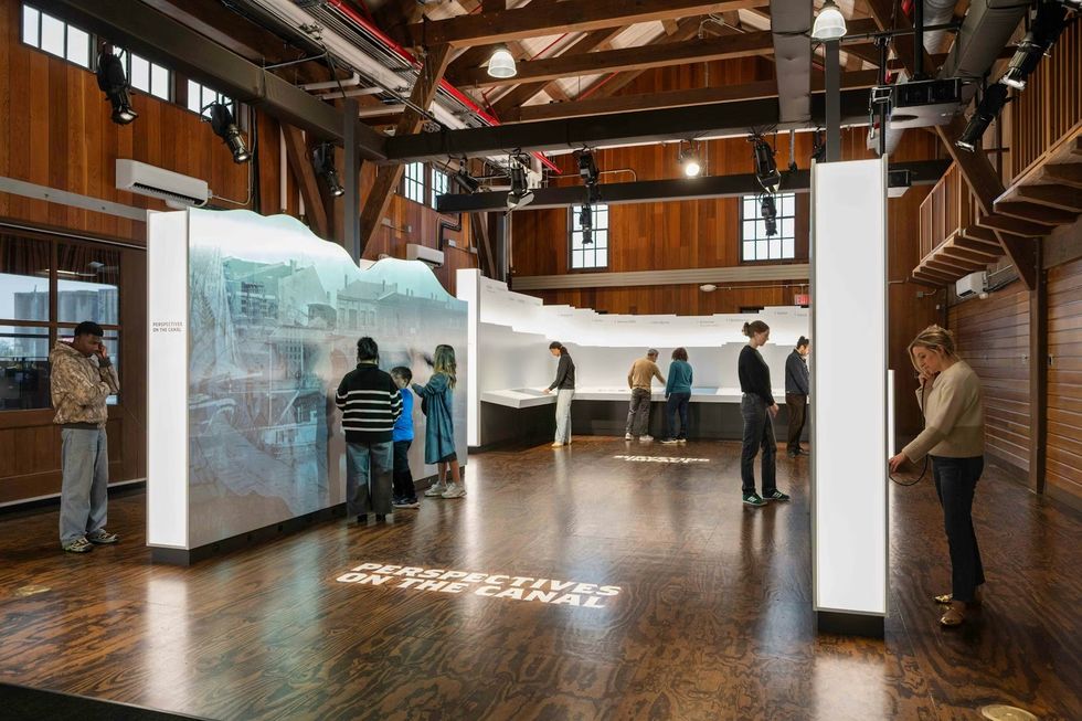 The Erie Canal Bicentennial Experience People explore interactive exhibits in a wooden, loft-style gallery space.
