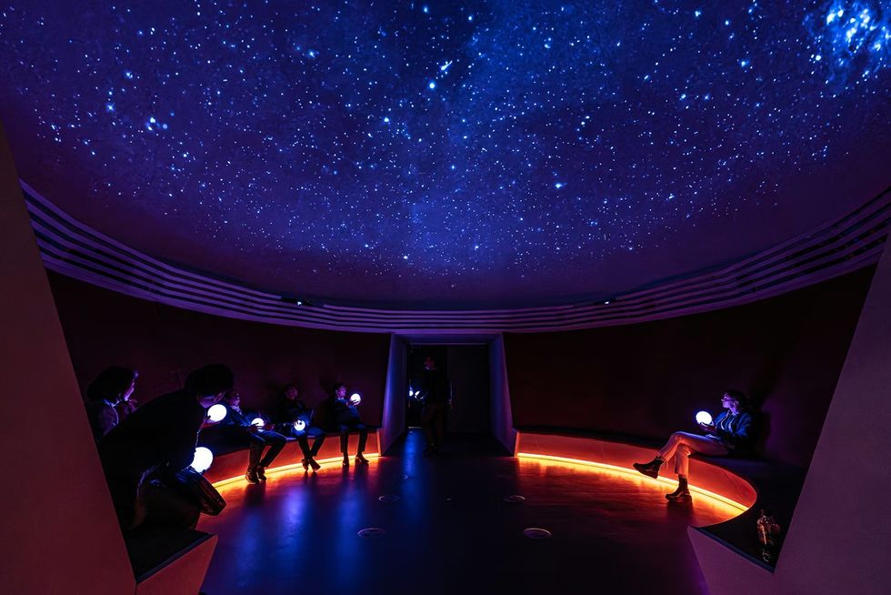 The Netherlands Pavilion at Expo 2025 People seated in a dark room under a starry dome, holding glowing spherical lights.