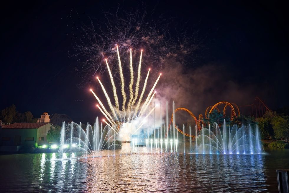 The nighttime spectacluar at Parc Asterix, with fireworks and illuminated fountains over a lake at night with a roller coaster in the background.
