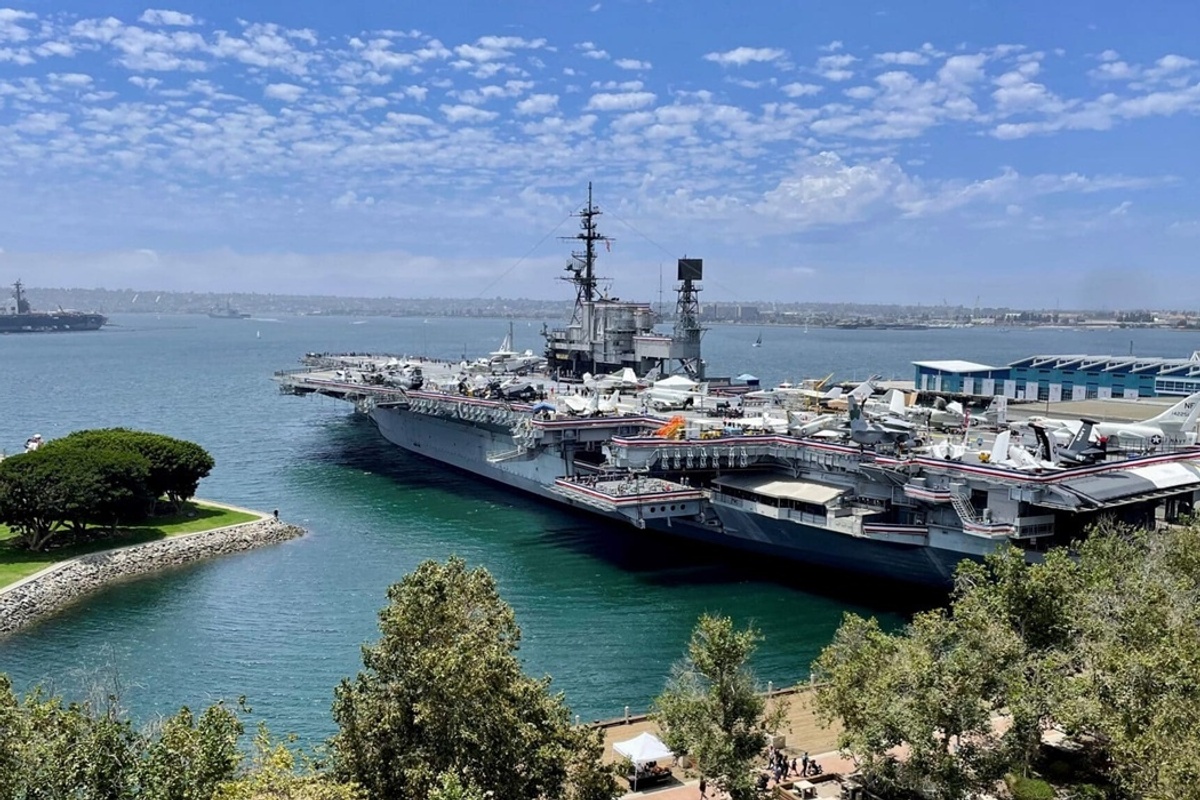 The USS Midway Museum, an aircraft carrier docked in a harbour with clear skies and surrounding greenery.