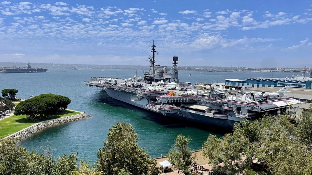 The USS Midway Museum, an aircraft carrier docked in a harbour with clear skies and surrounding greenery.
