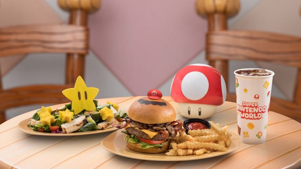 Themed food with burger, fries, star salad, and Super Nintendo World drink on a table.
