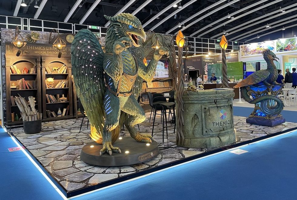 Themics IAAPA booth with a griffin statue and magical library backdrop.