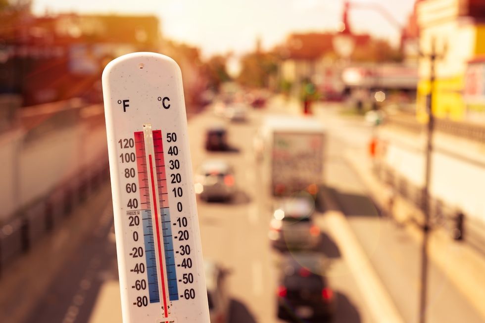 Thermometer reading high temperature against a busy city street background.