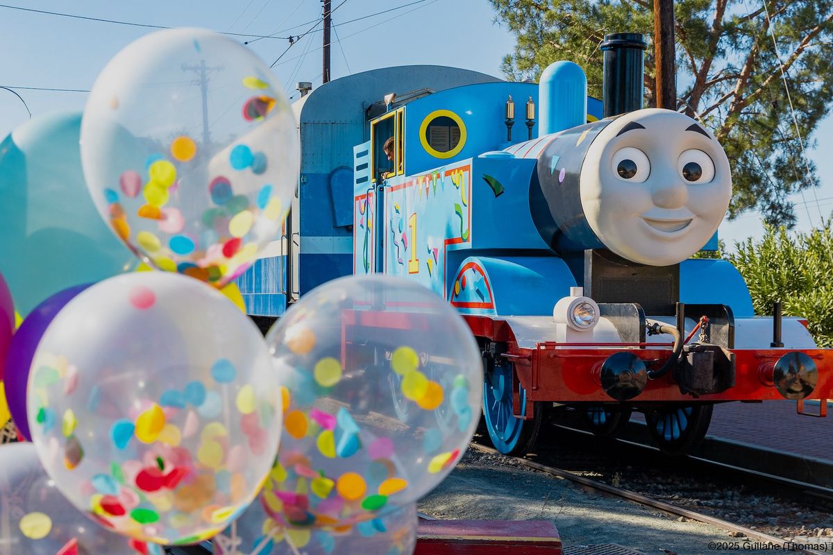 Thomas the Tank Engine character next to colorful balloons outdoors.