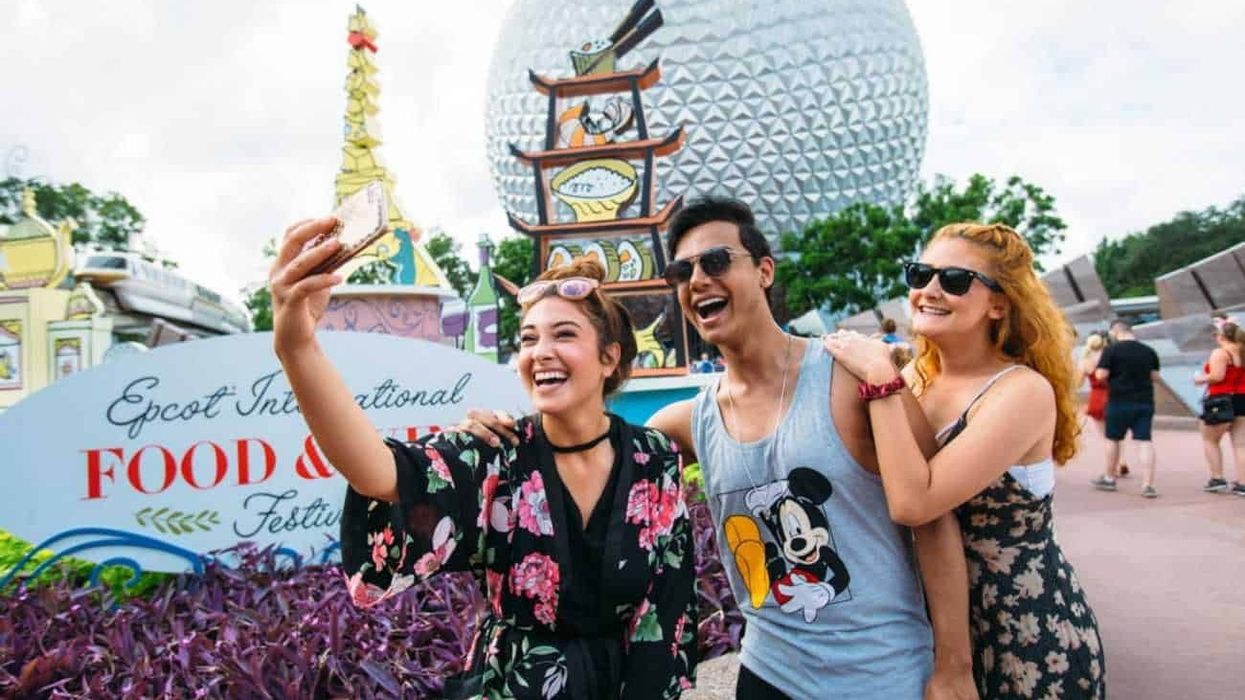 Three guests taking a photo in front of Epcot's International Food and Wine Festival 2018 signage