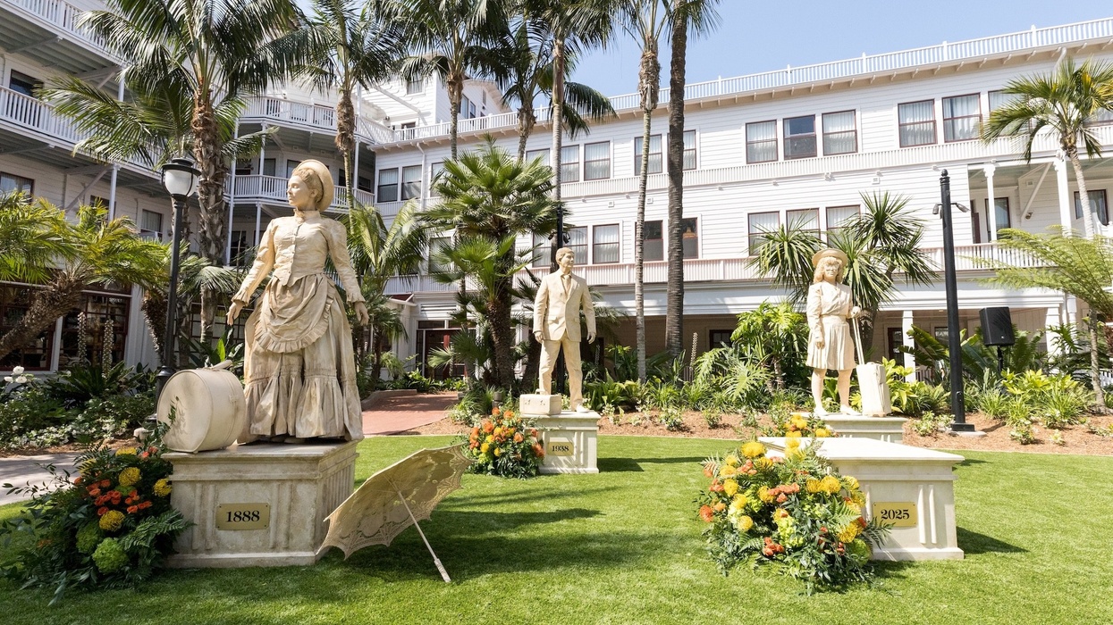 Three human statues in a garden area with palm trees and a white building.