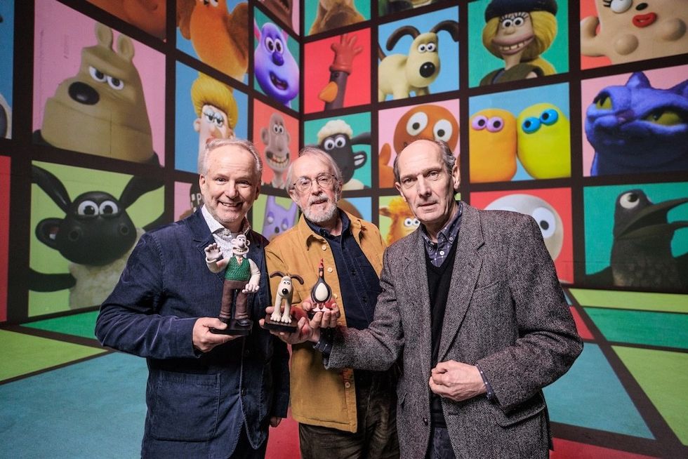 Three men holding Aardman claymation figures in front of a colorful cartoon character backdrop at Lightroom