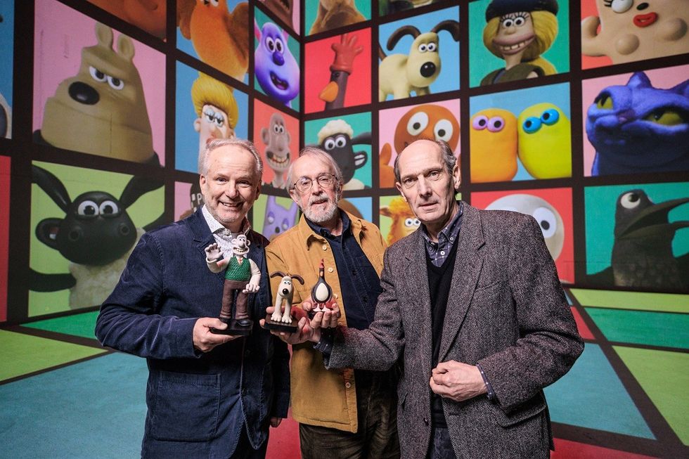 Three men holding claymation figures, colorful animated characters in the background.