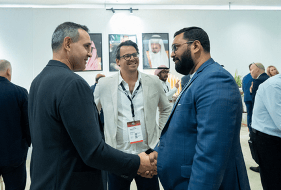 Three men in business attire smiling and shaking hands at a networking event.