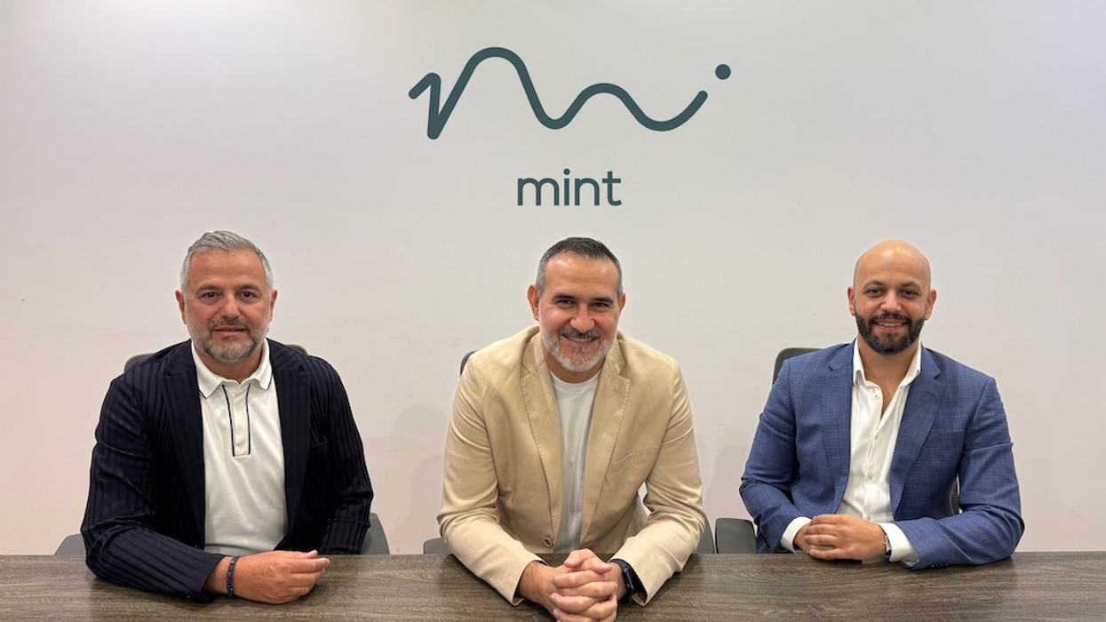 Three men sitting at a table with the Mint logo on the wall behind them.