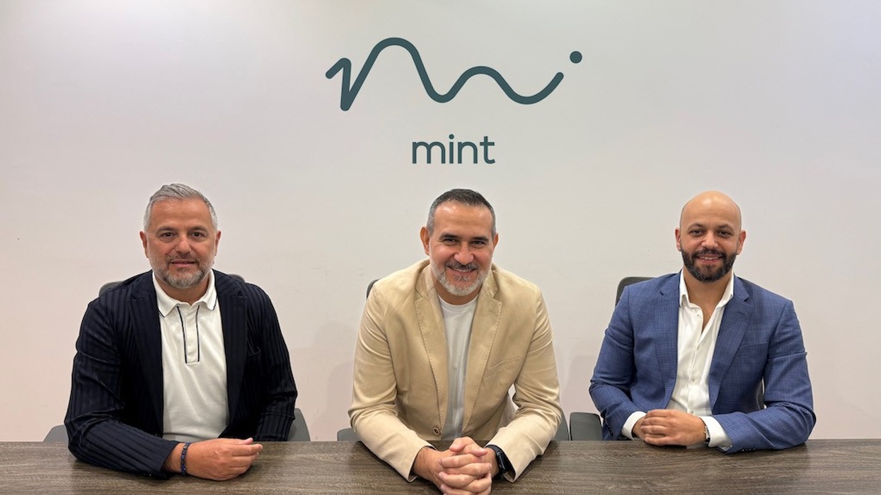 Three men sitting at a table with the Mint logo on the wall behind them.