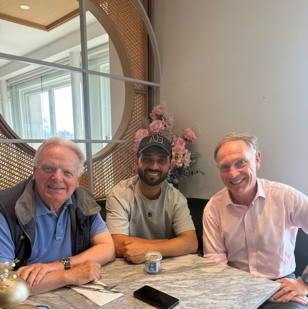 Three men smiling at a table with flowers in the background.