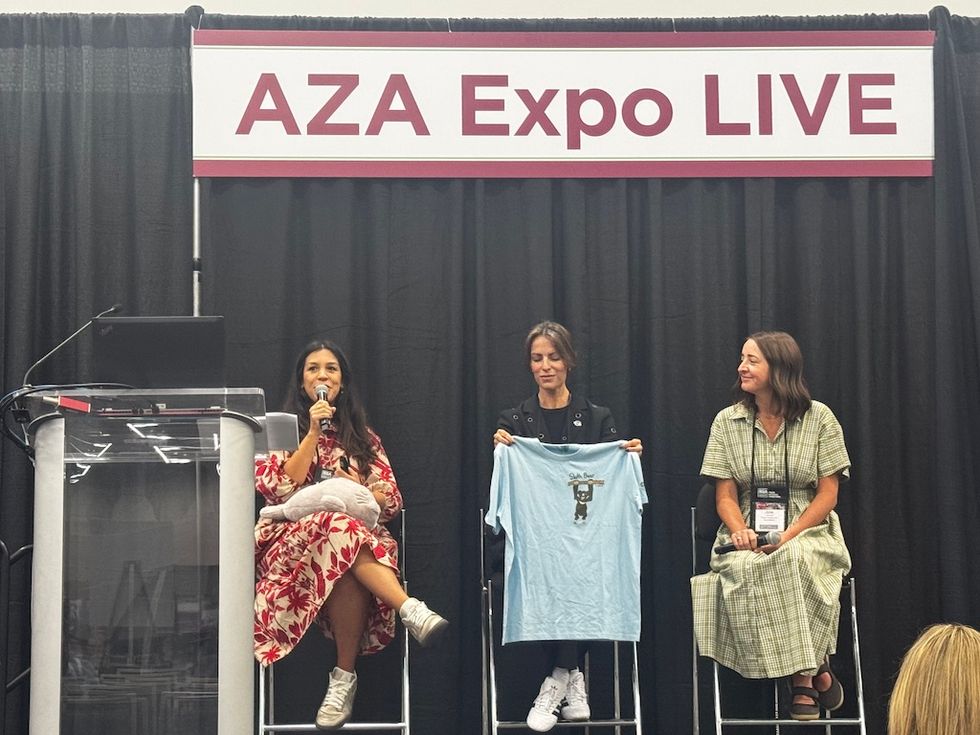 Three panelists on stage at AZA Expo LIVE, one holding a T-shirt.