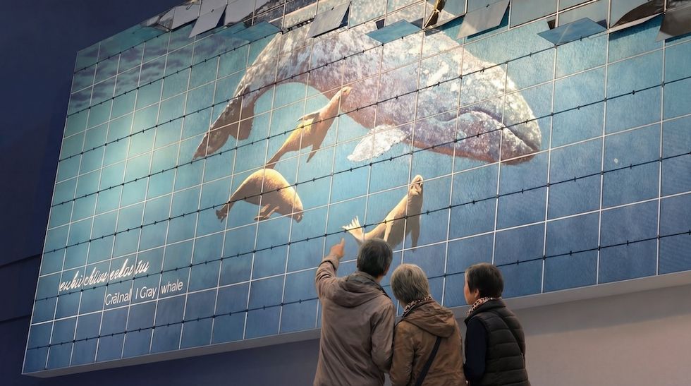 Three people admire a large gray whale mural on a tiled wall.