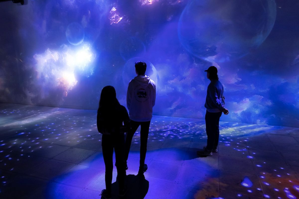 Three people admire immersive, colorful cosmic projections on a wall.