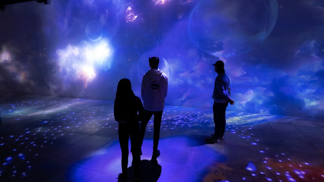 Three people admire immersive, colorful cosmic projections on a wall.