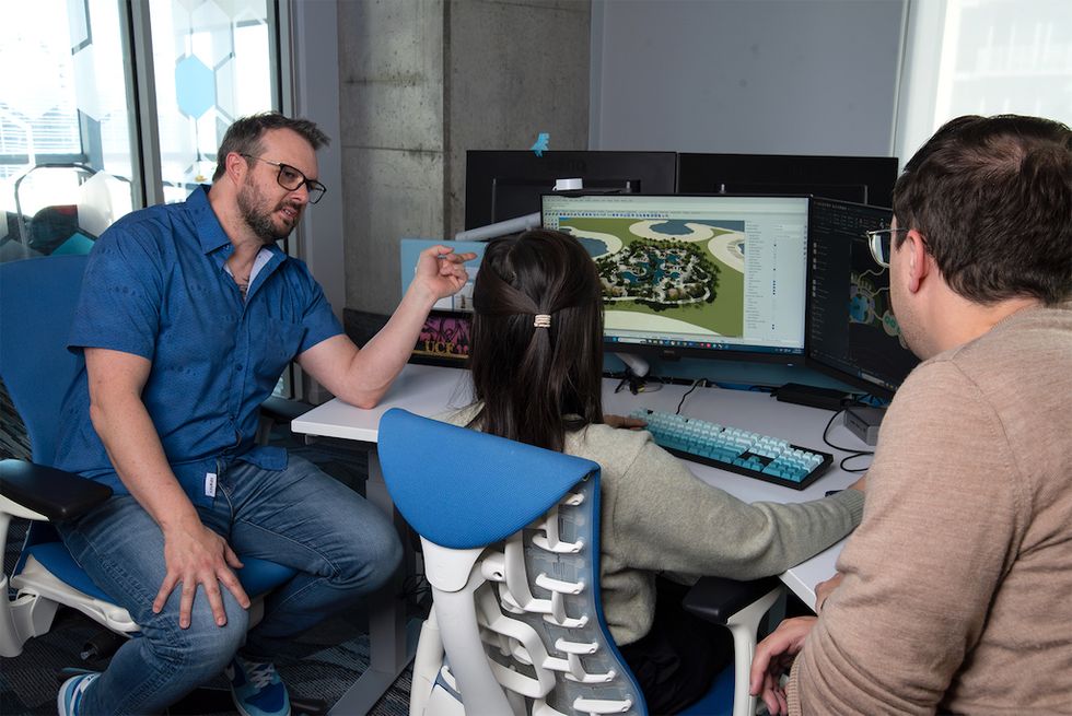Three people discuss a 3D landscape design on a computer screen.