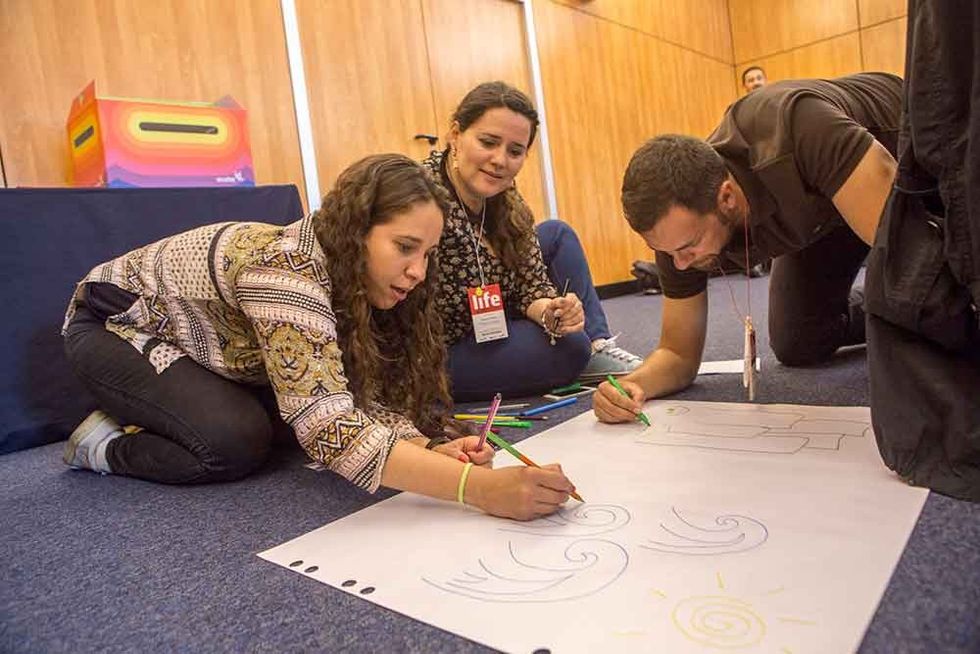 Three people drawing together on a large paper on the floor with colored markers at Ecsite event