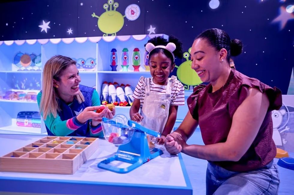 Three people enjoy playing with toys in a colorful, space-themed room at Peppa Pig Space Adventure
