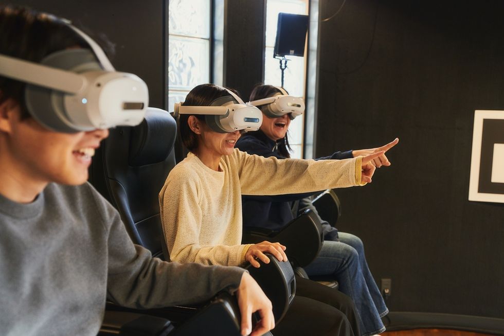 Three people enjoying a virtual reality experience titled 'AnimaLOOK!!', wearing VR headsets and pointing excitedly.
