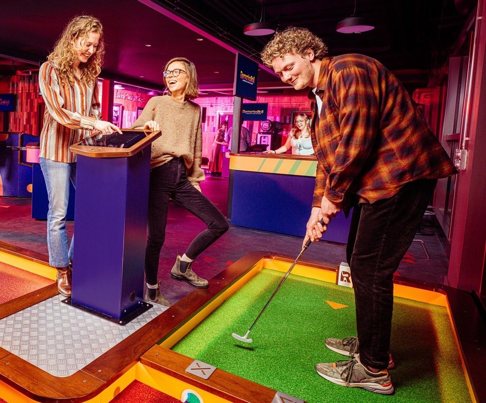 Three people enjoying an indoor minigolf game in a colorful venue.