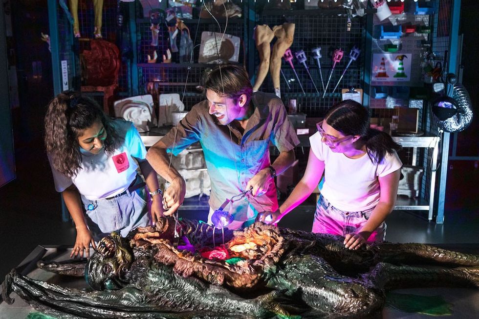 Three people examine an opened alien model with glowing lights in a workshop.