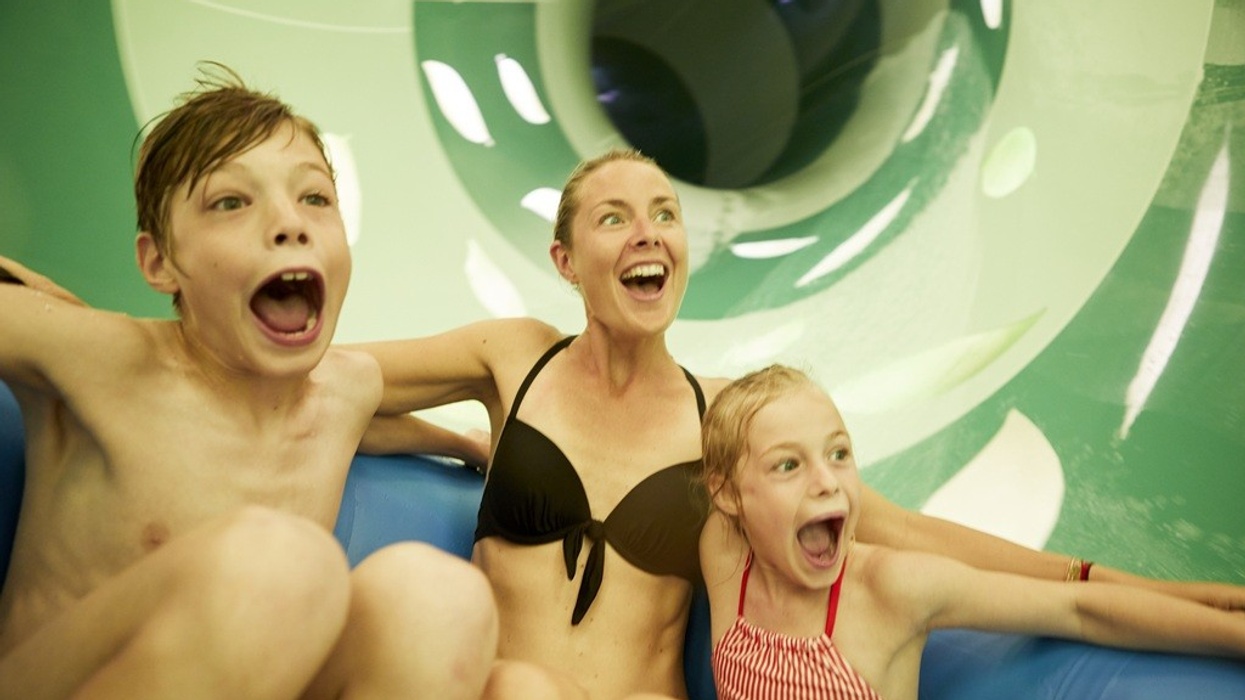 Three people excitedly sliding down a water slide together.