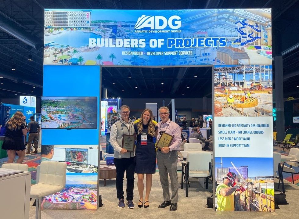 Three people holding awards in front of the "ADG Builders of Projects" booth display.