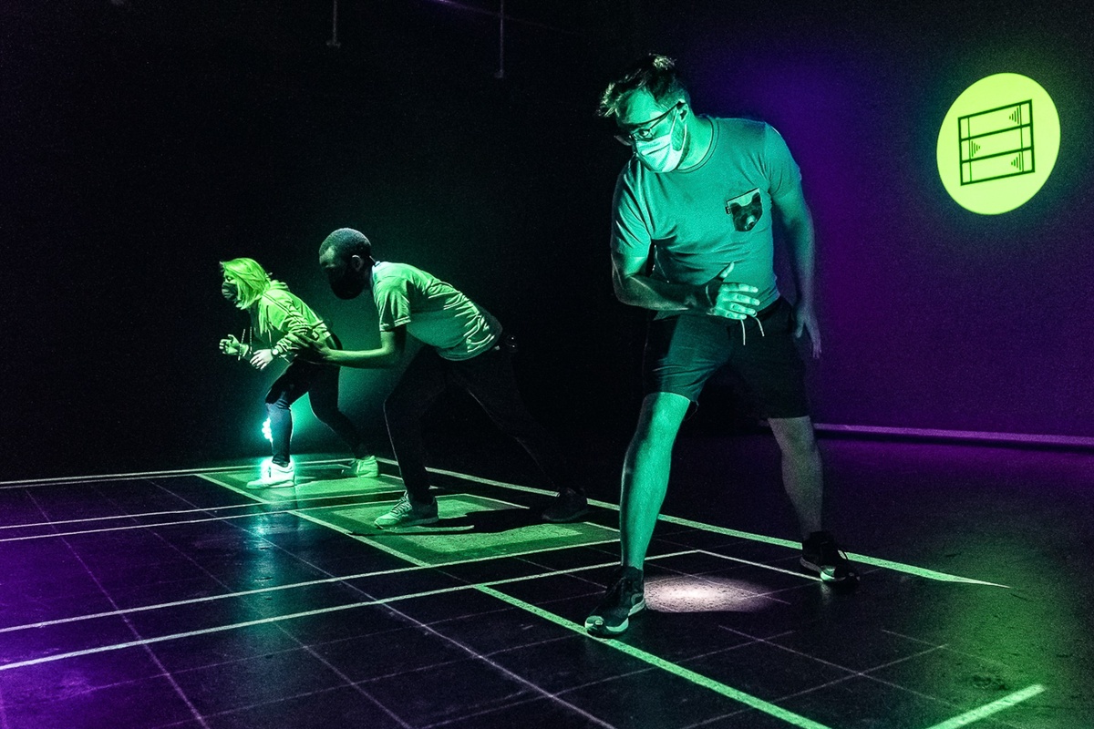 Three people illuminated by neon lights in a dark room, preparing to sprint.