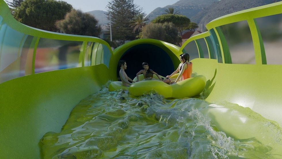 Three people in a raft on a green water slide, approaching a tunnel.
