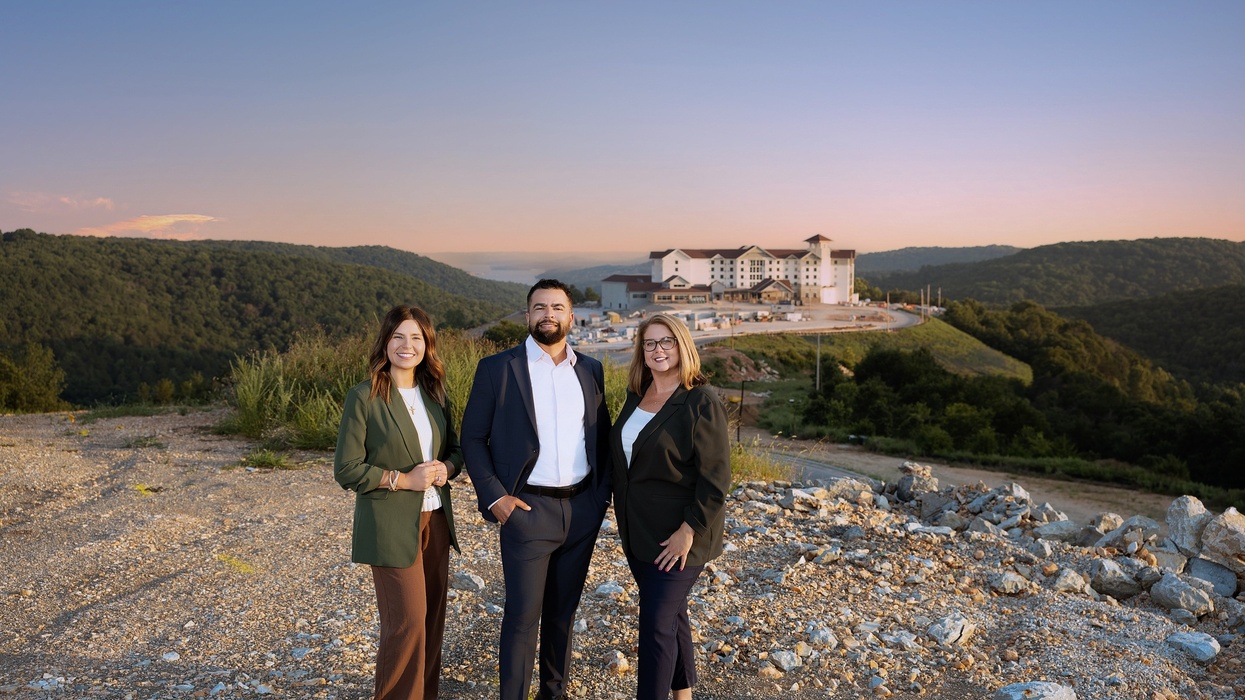 Three people in business attire stand on a hill, with Silver Dollar City Resort and mountains in the background.